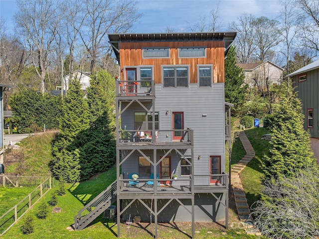 rear view of house with a balcony, a lawn, fence, and stairway