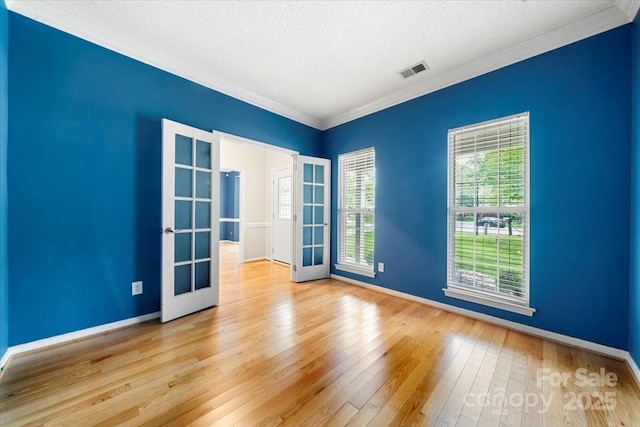 empty room with crown molding, hardwood / wood-style floors, french doors, baseboards, and visible vents