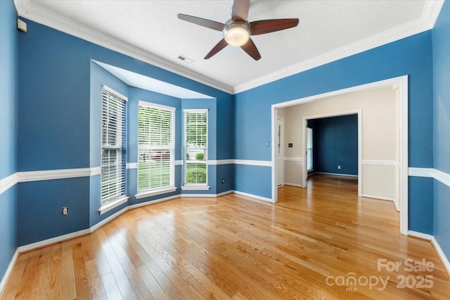 spare room with visible vents, a ceiling fan, wood-type flooring, crown molding, and baseboards
