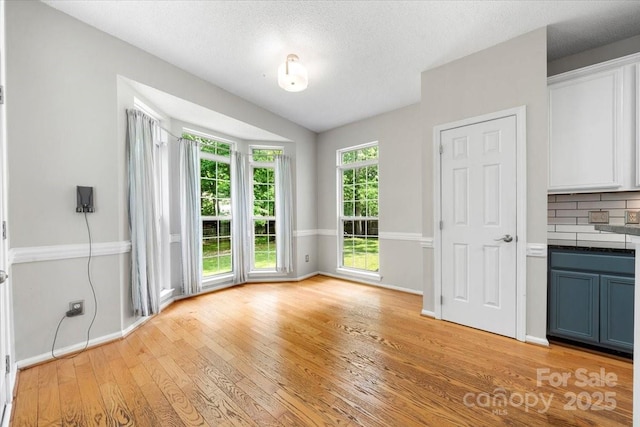 unfurnished dining area with baseboards, a textured ceiling, and light wood-type flooring