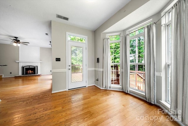 doorway featuring light wood-type flooring, baseboards, visible vents, ceiling fan, and a lit fireplace