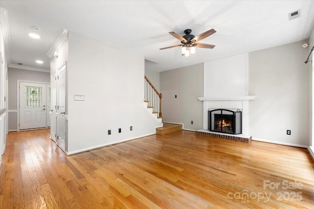unfurnished living room featuring stairway, a ceiling fan, light wood-style flooring, a fireplace, and visible vents