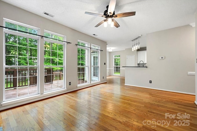 unfurnished living room with ceiling fan, a textured ceiling, visible vents, and light wood-style flooring