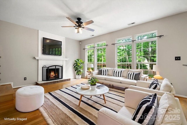 living room with a ceiling fan, wood finished floors, a lit fireplace, baseboards, and visible vents