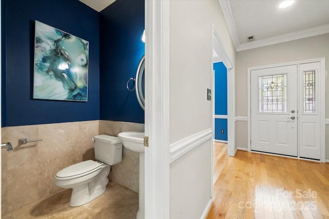 bathroom featuring toilet, tile walls, wainscoting, wood finished floors, and crown molding