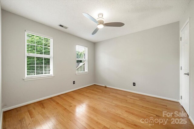 spare room featuring visible vents, a ceiling fan, baseboards, light wood-style flooring, and a textured ceiling