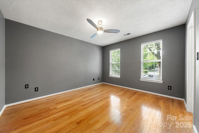 unfurnished room with a ceiling fan, a textured ceiling, light wood finished floors, baseboards, and visible vents
