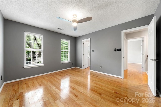 unfurnished bedroom featuring a textured ceiling, light wood-type flooring, baseboards, visible vents, and ceiling fan