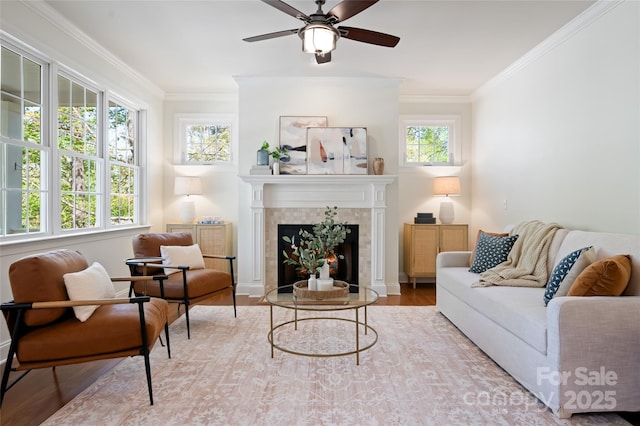 living room with a tiled fireplace, ceiling fan, a healthy amount of sunlight, and ornamental molding
