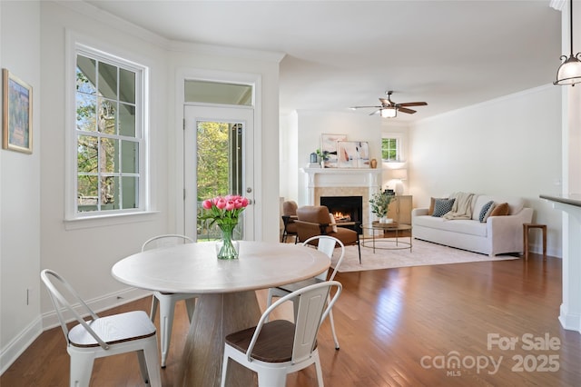 dining room with ceiling fan, a warm lit fireplace, wood finished floors, and baseboards