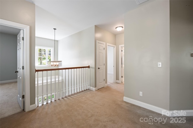 hallway with carpet floors, baseboards, and an inviting chandelier