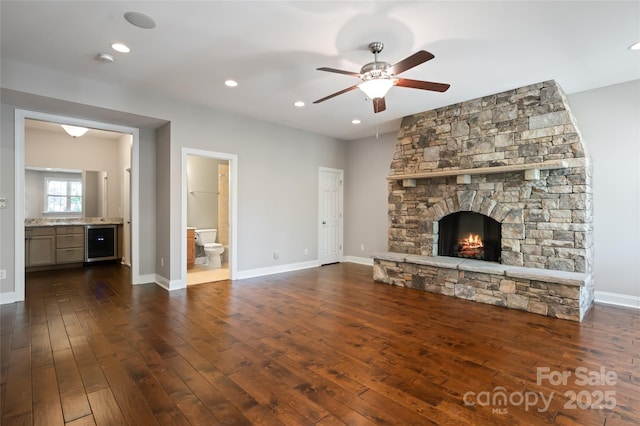 unfurnished living room featuring wine cooler, dark wood-style floors, baseboards, a ceiling fan, and a fireplace