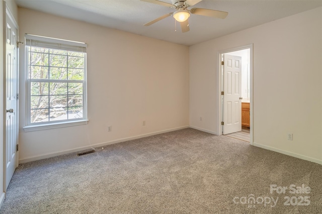 carpeted spare room with baseboards, a ceiling fan, a wealth of natural light, and visible vents