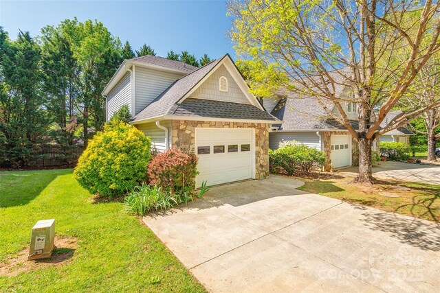 traditional home with roof with shingles, an attached garage, a front lawn, stone siding, and concrete driveway