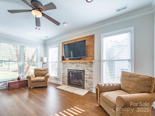 living room with ceiling fan, a fireplace, ornamental molding, visible vents, and wood finished floors