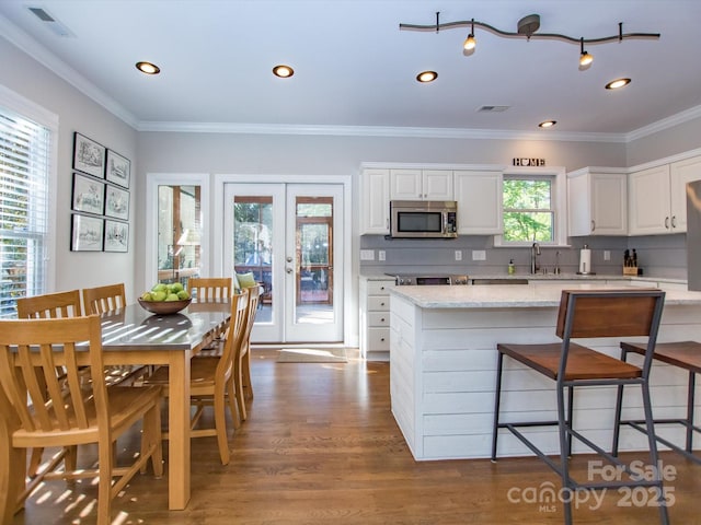 kitchen featuring ornamental molding, stainless steel microwave, wood finished floors, french doors, and backsplash