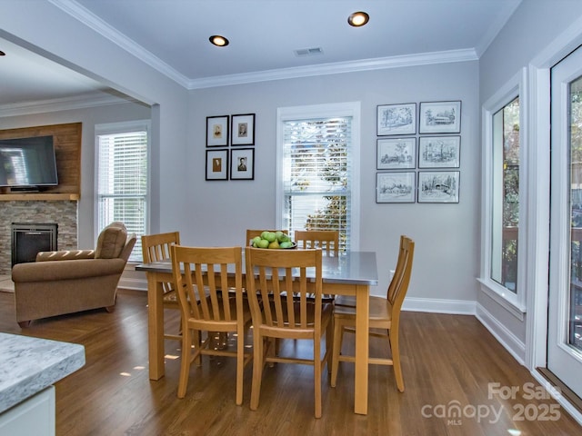 dining area with ornamental molding, a stone fireplace, visible vents, dark wood-style flooring, and baseboards
