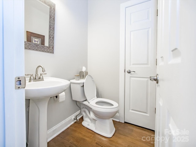 half bath with a sink, toilet, wood finished floors, and baseboards