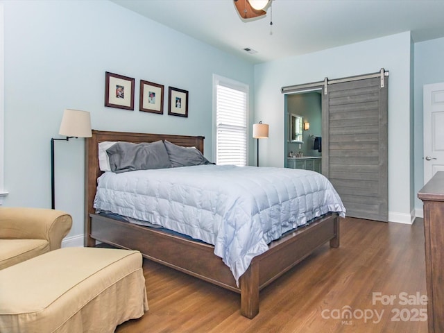 bedroom with baseboards, a barn door, visible vents, ceiling fan, and wood finished floors