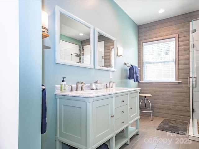 bathroom featuring wooden walls, tiled shower, tile patterned flooring, a sink, and double vanity