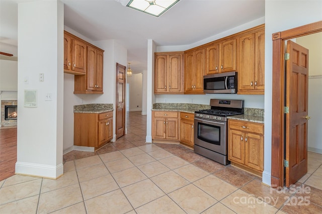 7900 Gilead Rd, Huntersville, NC 28078 - kitchen featuring stainless steel appliances, light stone counters, brown cabinetry, light tile patterned floors, and baseboards