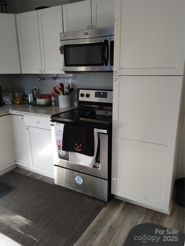 kitchen featuring stainless steel appliances, decorative backsplash, white cabinets, and wood finished floors