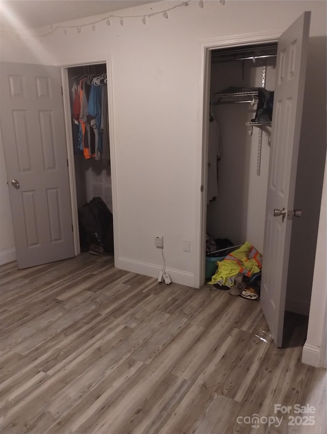 unfurnished bedroom with a walk in closet, a closet, baseboards, and wood finished floors