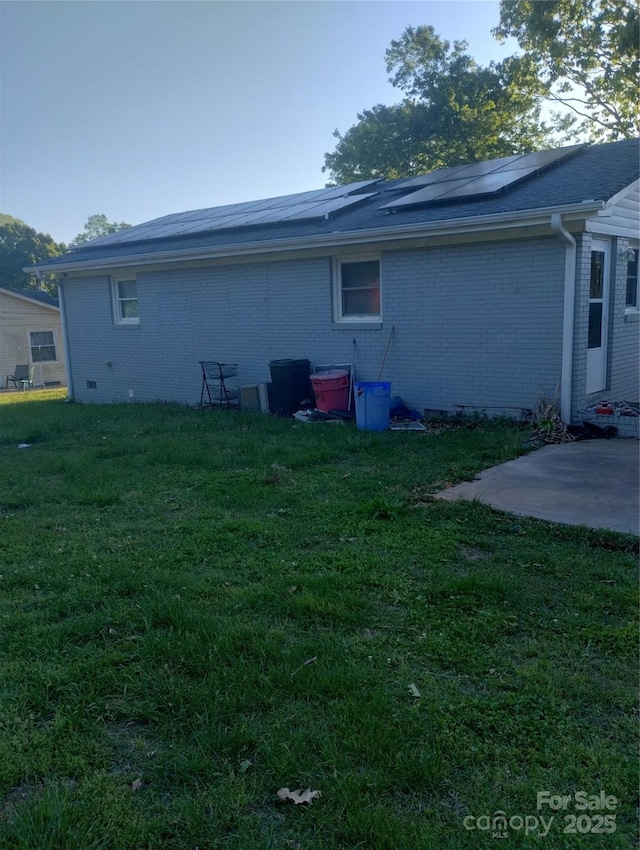 back of house with a lawn, brick siding, and solar panels