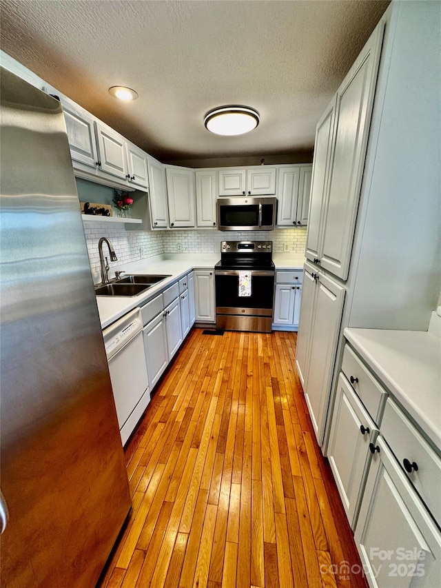 kitchen featuring a sink, stainless steel appliances, tasteful backsplash, light wood-style flooring, and light countertops