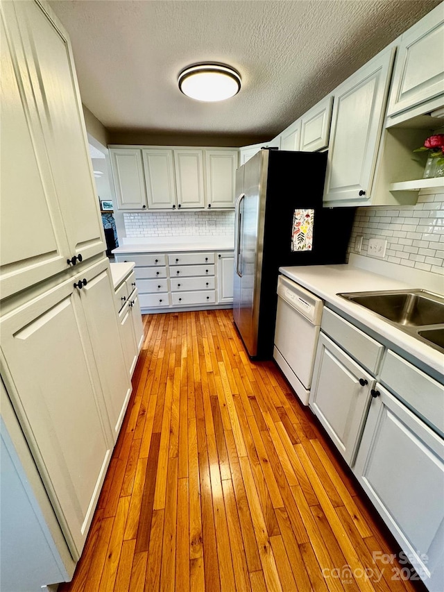 kitchen with light wood-style floors, backsplash, light countertops, dishwasher, and white cabinets