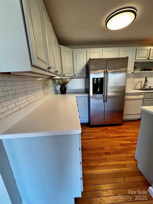 kitchen with tasteful backsplash, a sink, wood-type flooring, dishwasher, and stainless steel refrigerator with ice dispenser