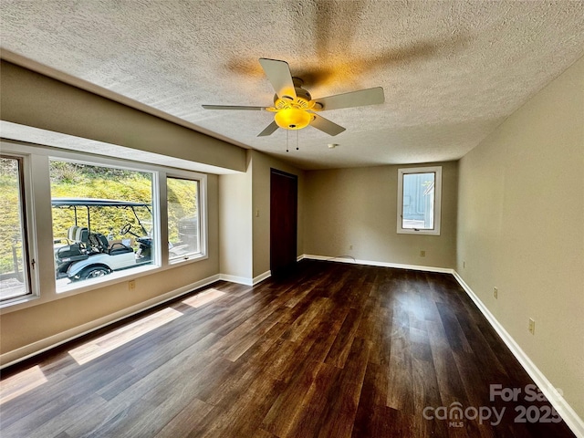 unfurnished room featuring a textured ceiling, a ceiling fan, baseboards, and dark wood finished floors