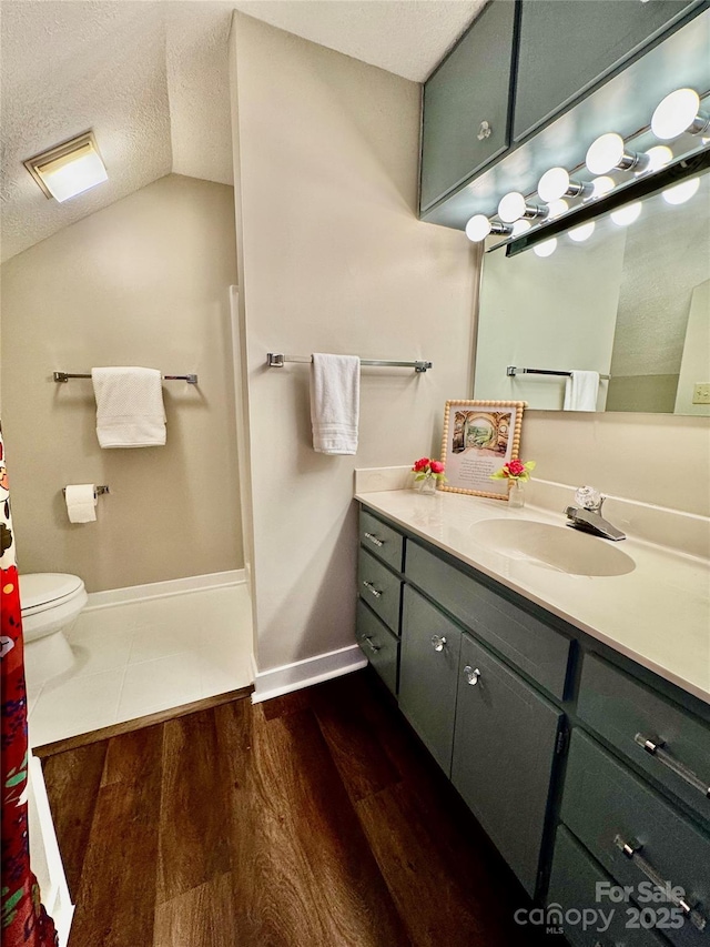 bathroom with vanity, vaulted ceiling, baseboards, a textured ceiling, and wood finished floors