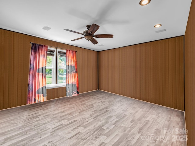 unfurnished room featuring wooden walls, light wood-style flooring, visible vents, and ceiling fan