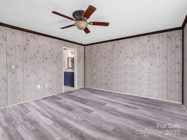 spare room with ceiling fan, ornamental molding, wood finished floors, and wooden walls