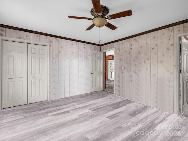 unfurnished bedroom with wood walls, wood finished floors, a closet, ceiling fan, and ornamental molding