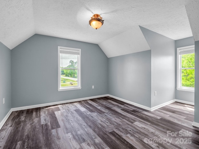 additional living space with baseboards, vaulted ceiling, wood finished floors, and a textured ceiling