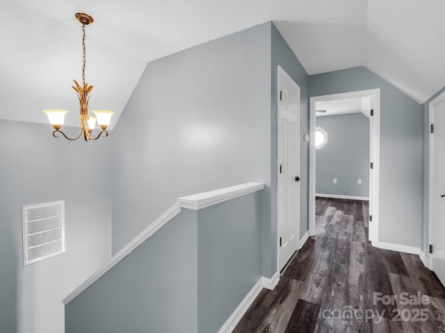 hallway featuring a chandelier, vaulted ceiling, wood finished floors, and an upstairs landing