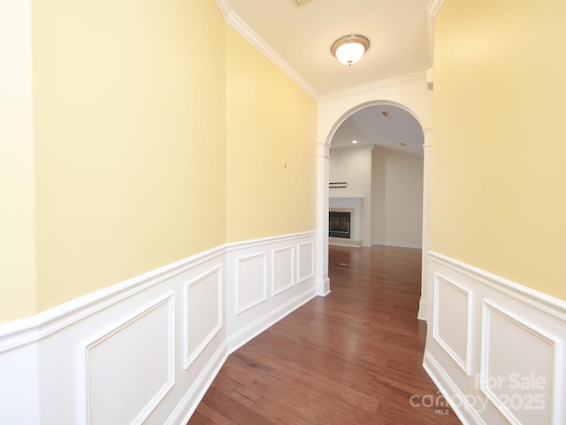 corridor with wood finished floors, arched walkways, a decorative wall, ornamental molding, and a wainscoted wall