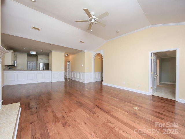 unfurnished living room with a ceiling fan, light wood-style flooring, vaulted ceiling, ornamental molding, and arched walkways