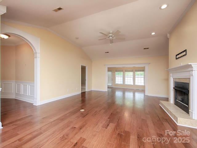 unfurnished living room with a fireplace with raised hearth, arched walkways, visible vents, and ceiling fan