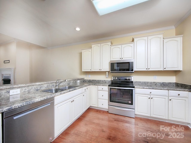kitchen featuring light wood finished floors, stainless steel appliances, ornamental molding, and a sink