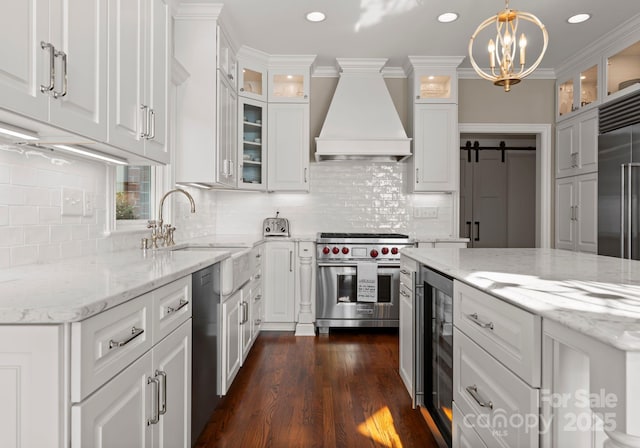 kitchen with a sink, a chandelier, custom range hood, white cabinetry, and appliances with stainless steel finishes