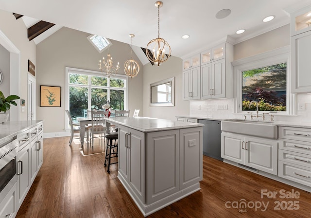 kitchen featuring stainless steel dishwasher, a sink, a kitchen island, dark wood-type flooring, and a notable chandelier