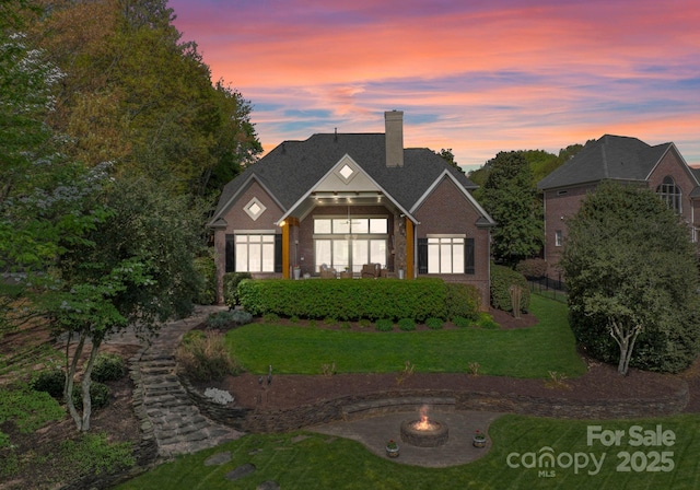 view of front facade with a chimney, a yard, brick siding, and an outdoor fire pit