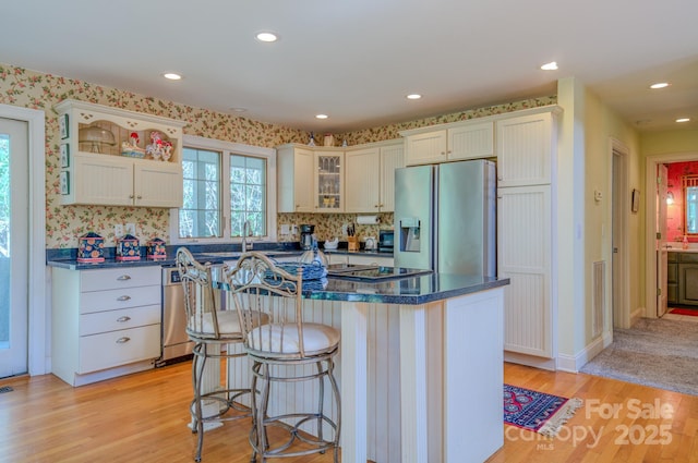 161 Hamburg Mountain Rd, Weaverville, NC 28787 - kitchen featuring appliances with stainless steel finishes, light wood-style floors, glass insert cabinets, a kitchen island, and a breakfast bar