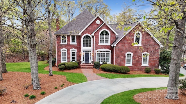 view of front facade with a front lawn, brick siding, and curved driveway