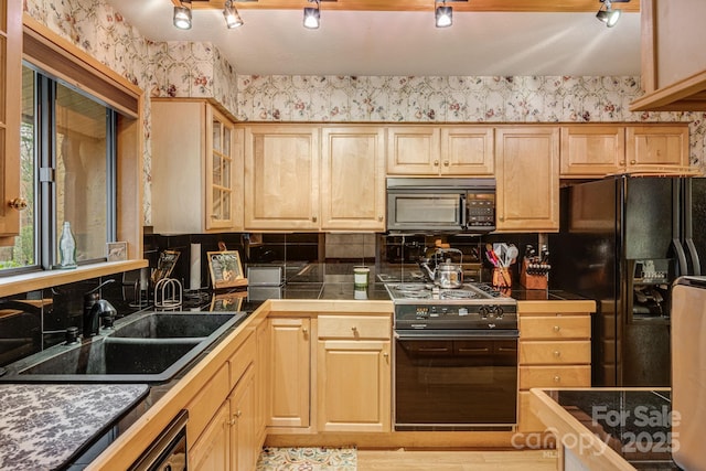 kitchen with wallpapered walls, a sink, tile countertops, light brown cabinets, and black appliances