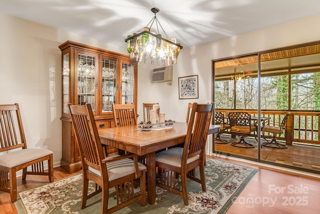dining space featuring a wall mounted air conditioner, wood finished floors, and an inviting chandelier