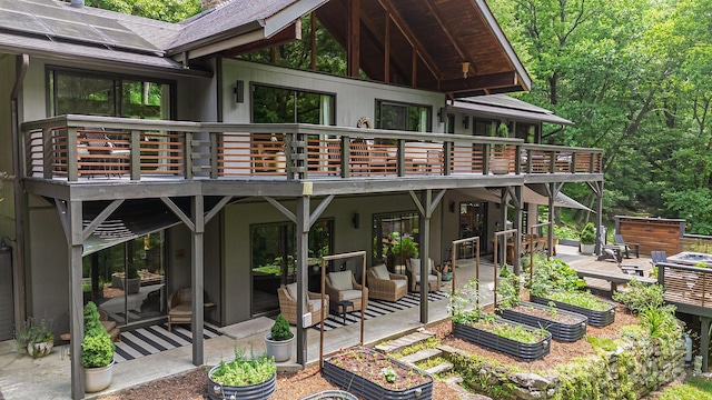 rear view of house with a patio area, a deck, solar panels, and a shingled roof